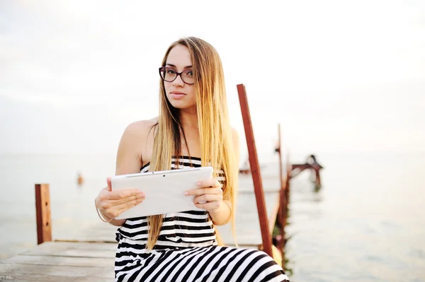 Chica con gafas en un vestido a rayas con una tableta de ordenador en h — Foto de Stock