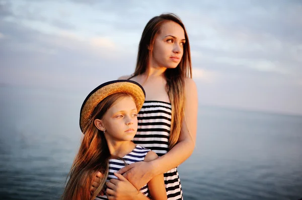 Duas meninas em pano listrado no fundo por do sol no mar — Fotografia de Stock