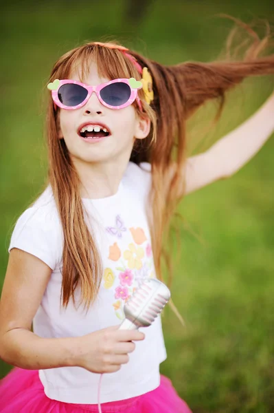 Menina ruiva alegre em óculos de sol cantando em um microfone — Fotografia de Stock