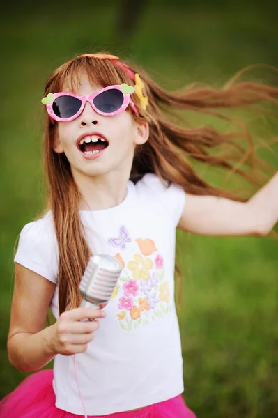 Menina ruiva alegre em óculos de sol cantando em um microfone — Fotografia de Stock