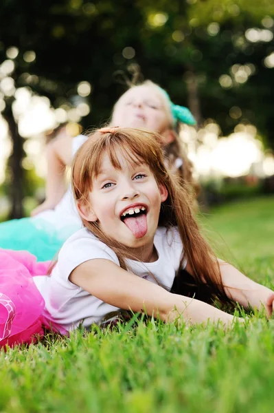 Twee kleine meisjes grimas op het gras-achtergrond — Stockfoto