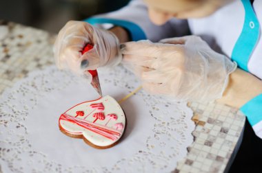 Pastry girl decorates a gingerbread heart. Valentine for Valentine's Day clipart