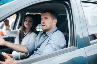 Bayan eğitmen yolda elinde bir şey gösteriyor ve tavsiye veriyor. Erkek öğrenci öğretmenini dinliyor. Konsantrasyon ve direksiyonla geleceğe bakıyor. Sürücü okulu konsepti.