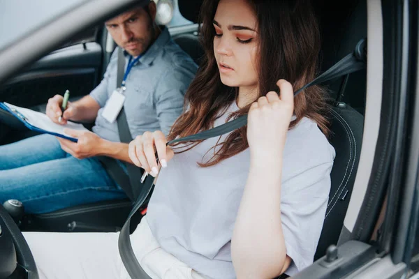 Vonzó fiatal nő ideges vezetés előtt teszt, biztonsági öv bekapcsolása és néz le. Férfi autós oktató értékeli a női tanulókat. Vezetői leckék. Vezetői engedély megszerzése. — Stock Fotó