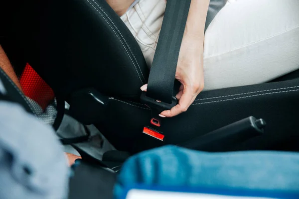 La mano femminile allaccia la cintura di sicurezza. Vista ravvicinata della donna in jeans bianchi con cintura di sicurezza nera. Il concetto di sicurezza stradale. Concetto di guida consapevole. — Foto Stock