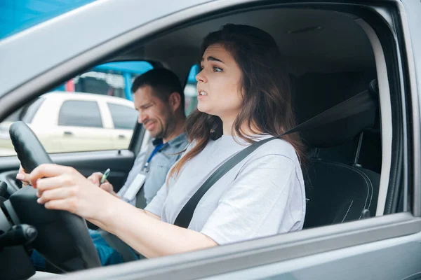 Zenuwachtige overstuur vrouw kan geen rijexamen doen. Auto-ongeluk tijdens rijles concept. Ontevreden mannelijke instructeur merkt iets slechts in zijn krant. Mislukt rijbewijsconcept. — Stockfoto