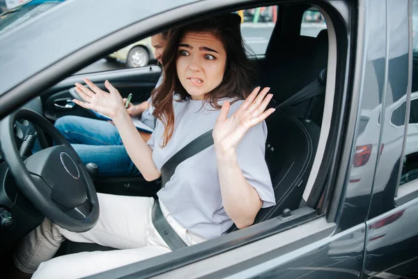 Bella giovane donna è turbata con i risultati della lezione di guida. Attraente donna confusa scrolla le spalle o compie un gesto indifeso dopo aver commesso un errore. Concetto di conducente principiante. — Foto Stock