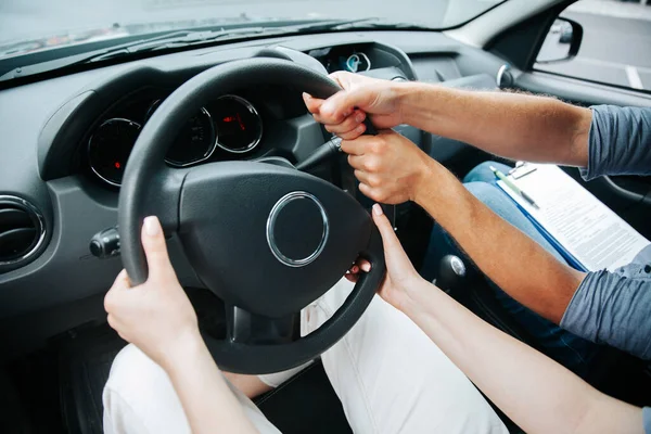 Due coppie di mani girano il volante insieme. Studentessa ai corsi di guida tenere il volante e istruttore maschile la aiuta a guidare. Lezioni di guida concetto. Vista da vicino. — Foto Stock