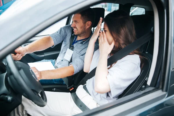 Instrutor de condução do sexo masculino tentando evitar uma colisão com outro carro. Uma jovem assustada cobre o rosto pelas mãos. O conceito de um exame de carta de condução com falha. — Fotografia de Stock