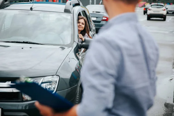 Uomo sfocato con appunti in mano si gira e guarda attraente giovane donna in auto grigia. donna caucasica sorride e lo invita a partecipare al viaggio. — Foto Stock