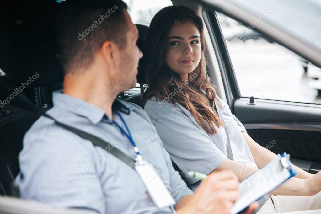 Male instructor praises attractive female student for driving successfully. Man writing something in paper and talking with pretty woman looking at him with respect.