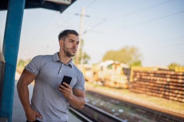 Tren istasyonunda cep telefonu kullanan yakışıklı adam. İletişim konsepti.