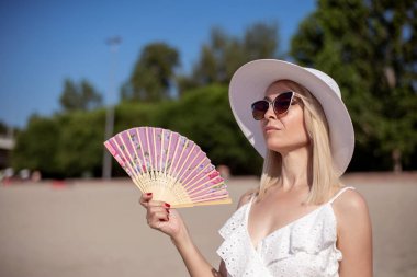 Kumsalda gülümseyen ve yelpaze tutan mutlu orta yaşlı kadın. Tatil canlılığı sağlıklı yaşam konsepti