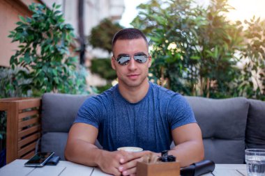 Yakışıklı ve başarılı bir adamın portresi kafede oturup kahve içiyor. Adamın biri güzel bir terasta oturmuş bitkilerle kahvaltı yapıyor..