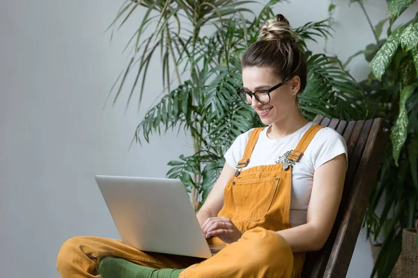 Ung Kvinnlig Trädgårdsmästare Glasögon Overaller Sitter Trästol Växthus Använder Bärbar — Stockfoto