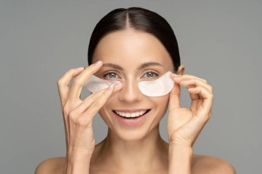 Happy woman applying hydrogel under-eye recovery patches enriched with collagen, vitamin E, provides intensive hydration and diminishes the signs of aging, helps reduse eye puffiness. Skincare beauty. clipart