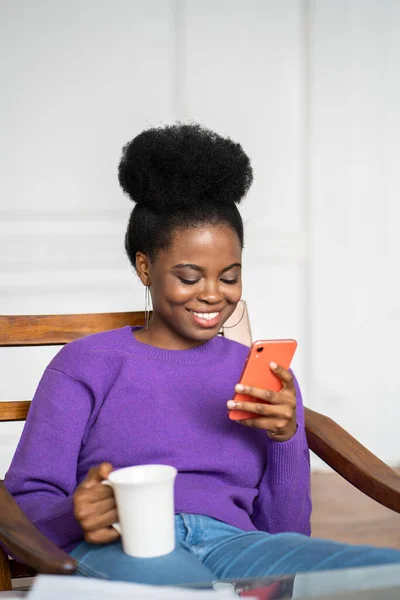 밀레니엄 여성은 보라색 스웨터를 의자에 전화를 사용하고 네트워크에서 수다를 커피를 — 스톡 사진