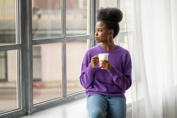 귀걸이를 포괄적 아프리카계 미국인 여성은 보라색 스웨터를 머그를 커피나 마시며 — 스톡 사진