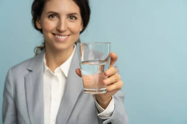 Jeune femme d'affaires en blazer gris posant sur fond bleu studio isolé, tenant verre d'eau minérale — Photo