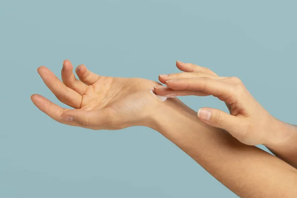 Vrouw die beschermende crème aanbrengt op de droge huid van de handen in het koude seizoen, geïsoleerd op studio blauwe achtergrond — Stockfoto