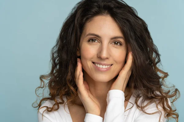 Ung kvinna med naturlig makeup, lockigt hår, vidrör välvårdad ren hud i ansiktet, isolerad — Stockfoto