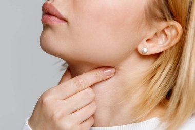 Close up of woman touches fingers of sore throat, isolated on gray background. Thyroid gland, painful swallowing, tonsillitis, laryngeal swelling concept. Inflammation of the upper respiratory tract clipart