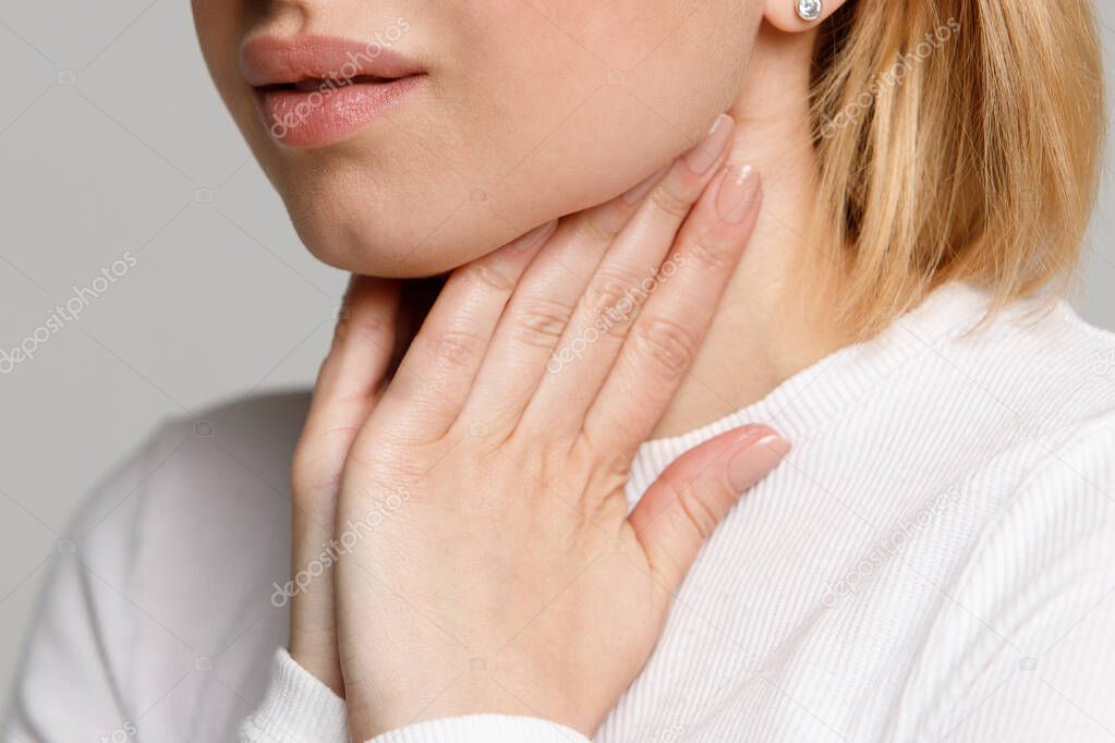 Closeup of sick young woman suffering from throat problems, holding hands on her lymph nodes, isolated. Thyroid gland, painful swallowing concept. Inflammation of the upper respiratory tract