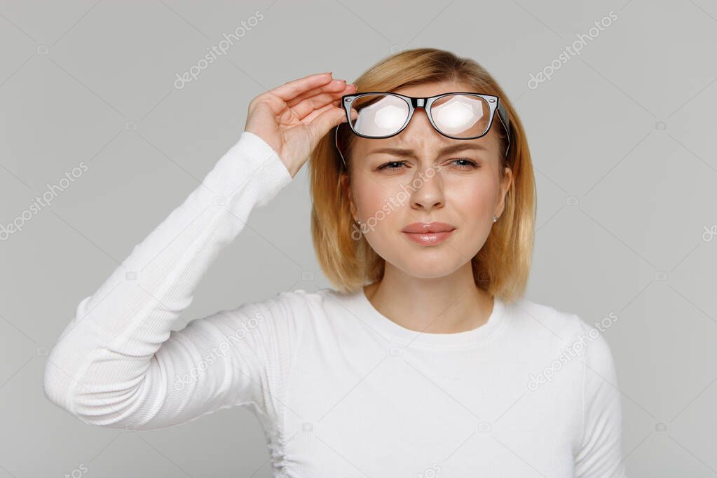 Woman has problems with poor eyesight, squinting while trying to see something, takingoff glasses, isolated on gray background. Myopia, hyperopia, vision concept.