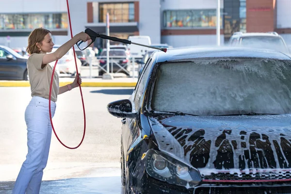 白人の若い女性のドライバーは 手動車の洗浄では 泡で洗浄し 圧力の水を洗う 高圧ホース付きセルフサービス車の洗浄 — ストック写真