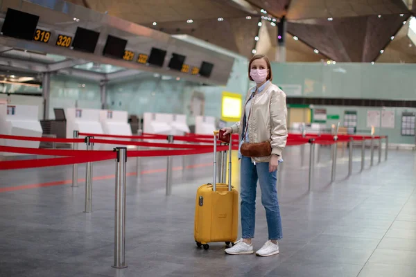 Woman with luggage stands at almost empty check-in counters at the airport terminal due to coronavirus pandemic/Covid-19 outbreak travel restrictions. Flight cancellation.Quarantine all over the world