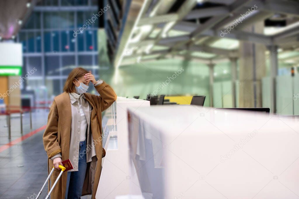 Woman with luggage upset over flight cancellation, stands at empty check-in counters at the airport terminal due to coronavirus pandemic/Covid-19 outbreak travel restrictions. Quarantine measures.