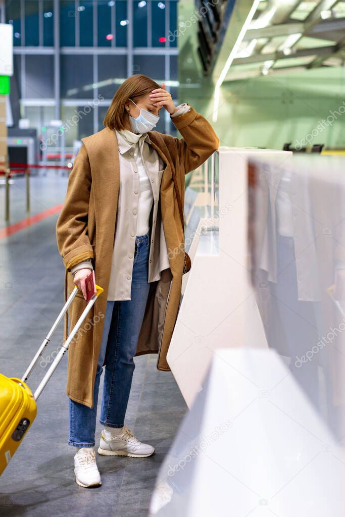 Woman with luggage upset over flight cancellation, stands at empty check-in counters at the airport terminal due to coronavirus pandemic/Covid-19 outbreak travel restrictions. Quarantine measures. 