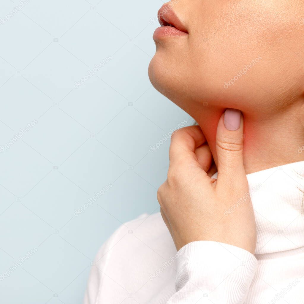 Close up of woman touches fingers of sore throat, isolated on blue background. Thyroid gland, painful swallowing, tonsillitis, laryngeal swelling concept. Inflammation of the upper respiratory tract