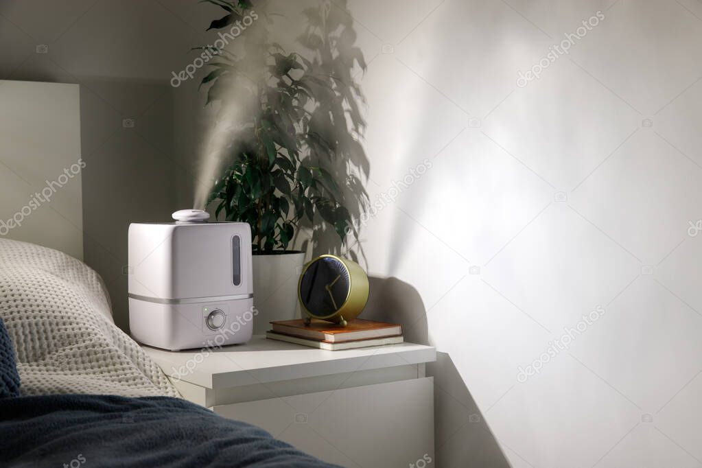 Aroma oil diffuser on the bedside table at night at home, steam from the air humidifier. Ultrasonic technology, increase in air humidity indoors. 