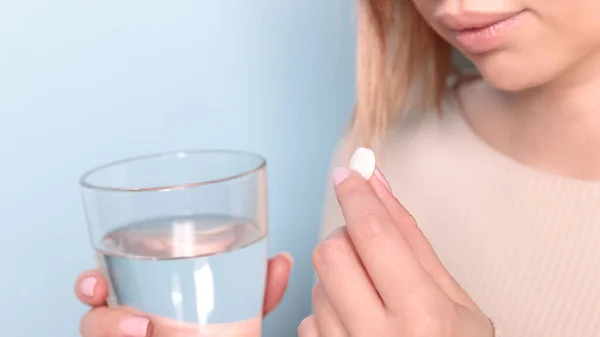 錠剤と水のガラスを服用不健康な若い女性のクローズアップ 青の背景 — ストック写真