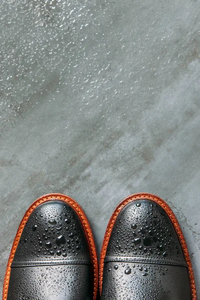 Top view of black leather men boots with water drops on grunge navy blue background, copy space, flat lay. Warm shoes for autumn weather.