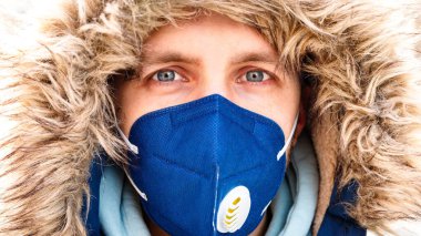 Kapüşonlu adamın solunum cihazı N95 maskesi takması ve grip, coronavirus / covid-19 'u korumak için toplu taşımada kameraya bakması.