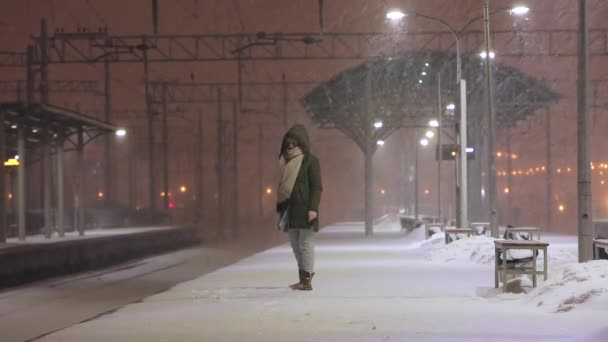 Женщина на пустой железнодорожной платформе в снежную бурю ждет поезда. Девушка опоздала на поезд — стоковое видео