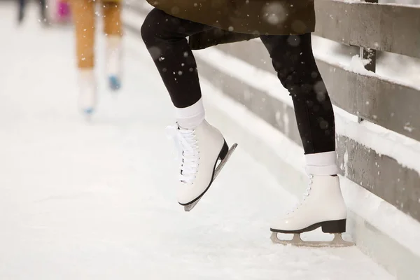 Close up of woman skater legs at open skating rink, side view. Female white skates on ice, trains near the wall, learning to balance. Weekend activities outdoor in cold weather.
