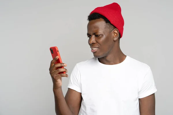 Confus homme hipster africain regardant mobile, ennuyé par le spam, adware intrusif message désagréable — Photo