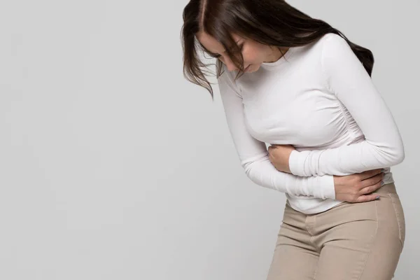 有胃痛 月经痛或抽筋的年轻妇女在灰色背景下被隔离的工作室肖像 慢性胃炎 女性健康问题 肚子痛和妇科病 — 图库照片