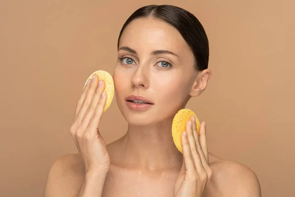 Ung kvinna med naken make-up och nakna axlar rengör ansiktet med exfolierande svamp isolerad — Stockfoto