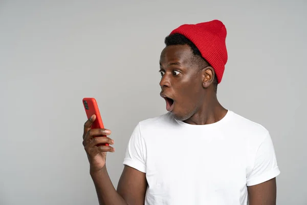 Překvapený afro muž dělá velké oči otevře ústa široce, šokován neslušné fotografie, při pohledu na mobilní — Stock fotografie