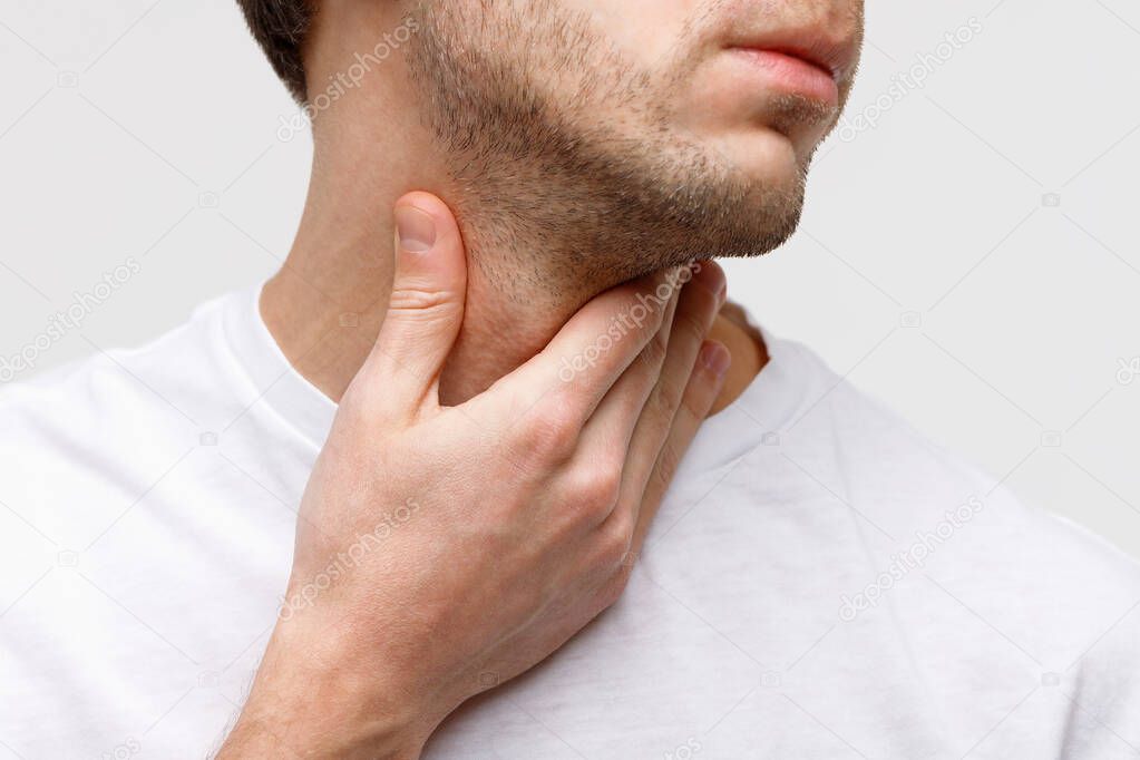 Close up of sick man suffering from throat problems, grey background, isolated. Thyroid gland, painful swallowing, pharyngitis, laryngeal swelling concept. Inflammation of the upper respiratory tract