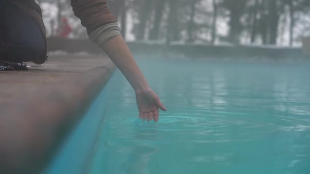 La mano de la mujer que comprueba la temperatura del agua en la piscina abierta en invierno. Spa termal al aire libre. — Vídeos de Stock