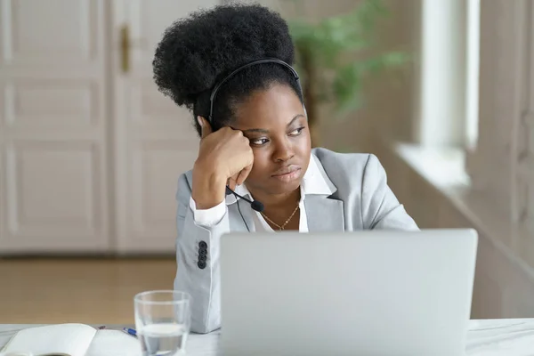 Nachdenkliche Afro-Geschäftsfrau trägt Kopfhörer, schaut zum Fenster, arbeitet im Büro am Laptop. — Stockfoto