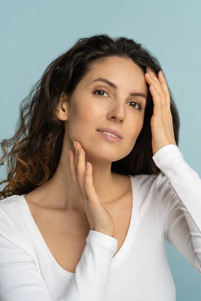 Mujer joven con maquillaje natural, pelo rizado, tocando la piel pura bien arreglada en la cara, aislado — Foto de Stock