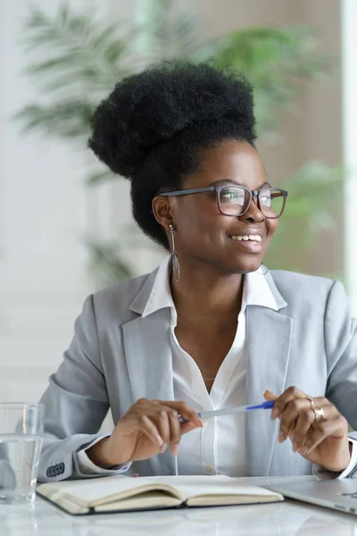 Smiling Afro woman in blazer wear glasses working at laptop computer at home office, looking away. — Stock Photo, Image