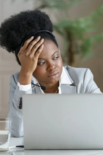 Omtänksam trött afro affärskvinna bära hörlurar tittar på fönstret, arbetar på laptop, närbild. — Stockfoto