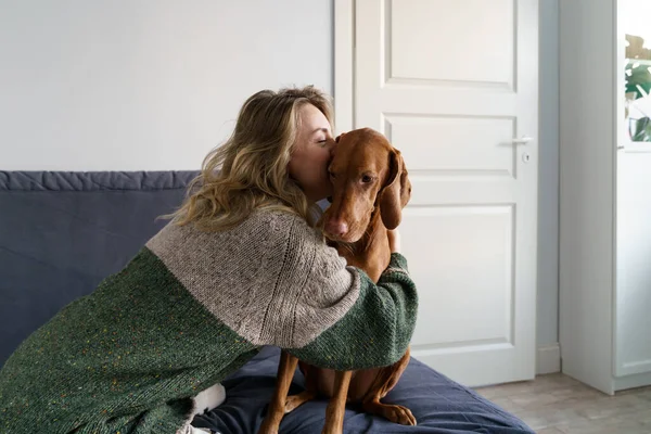 Femme en pull embrassant son chien bien-aimé Wirehaired Vizsla, assis sur le canapé à la maison. Amour animaux domestiques. — Photo